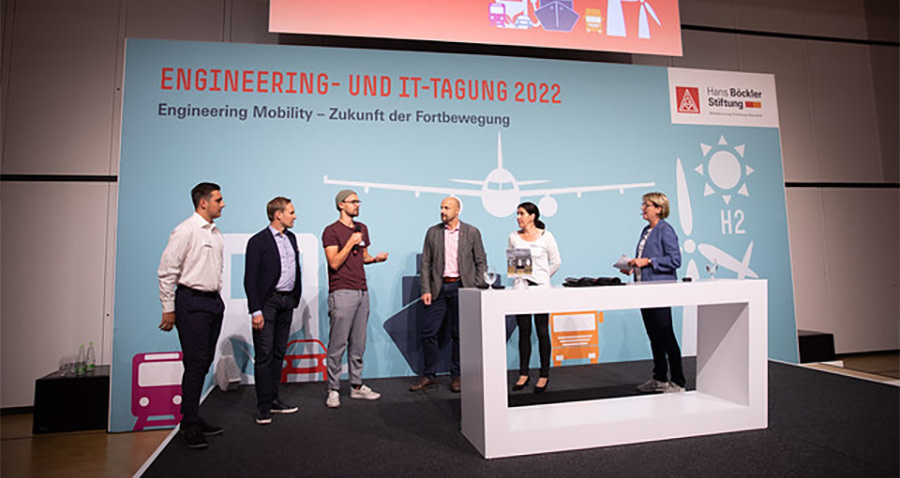 Menschen stehen auf einer Bühne, im Hintergrund ist auf einem Backdrop: `Engineering- und IT-Tagung 2022` zu lesen